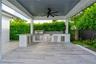 Covered outdoor kitchen featuring wood-finish tile flooring, built-in stainless steel grill, stone-style countertop, mosaic tile backsplash, and overh