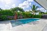 Rectangular swimming pool with a sun shelf, surrounded by light-toned stone decking, mature palm trees, and privacy fencing