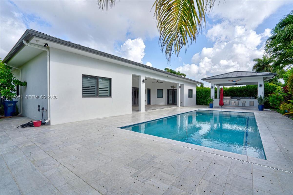 Backyard featuring a rectangular swimming pool, expansive stone-paver decking, covered patio, and a detached poolside pavilion with a built-in outdoor