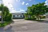 Single-story exterior featuring a metal roof, smooth stucco facade, expansive paved driveway, and mature landscaping