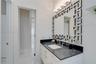 White vanity with dark stone countertop, undermount rectangular sink, chrome widespread faucet, geometric-patterned mirror, and four-light glass wall 