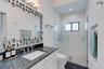 Glossy white cabinetry, dark stone countertop with an undermount sink, geometric mirror frame, walk-in glass-enclosed shower with chevron-patterned ti
