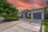 Modern single-story exterior featuring a geometric concrete paver driveway, covered entryway with column detailing, attached garage, and mature profes