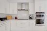 Kitchen featuring high-gloss white cabinetry, geometric patterned backsplash, stainless steel double wall oven, stainless steel range hood, and solid-