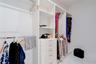 Custom walk-in closet featuring white built-in shelving, a central column of five soft-close drawers, stainless steel hanging rods, and polished stone