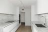 Galley kitchen featuring flat-panel white cabinetry, stone-surface countertops and backsplashes, built-in dual ovens, integrated cooktop, and wood-fin