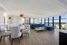 Open-concept living space featuring wood-finish flooring, floor-to-ceiling black-framed windows, and a decorative gold-finish pendant light