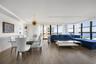 Open-concept interior featuring wood-finish flooring, floor-to-ceiling windows with water vistas, built-in recessed display shelving, and modern track