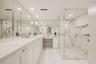 Dual-sink vanity with quartz countertop, expansive wall-to-wall mirrors, integrated makeup vanity station, and glass-enclosed walk-in shower featuring