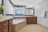 Bathroom featuring a corner soaking tub with tile surround, wood cabinetry, stone-finish countertops, ceramic tile flooring, and a large framed vanity