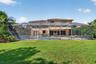 Rear exterior featuring a screened-in lanai with a swimming pool, built-in outdoor kitchen, concrete patio, and a fenced grass lawn