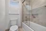 Bathroom featuring a sliding glass shower door, recessed wall niche, neutral stone-tile surround, and window with blinds