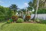 Backyard featuring a manicured lawn, established palm trees, ornamental shrubbery, and wood-panel fencing