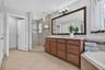 Bathroom featuring a natural wood-finish vanity with stone-surfaced countertop, glass-enclosed shower with tile surround, large framed wall mirror, an