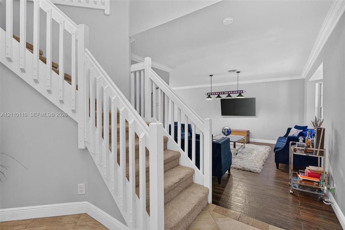 Staircase featuring white balusters and handrail, neutral-tone carpeting, wood-finish flooring, and crown molding