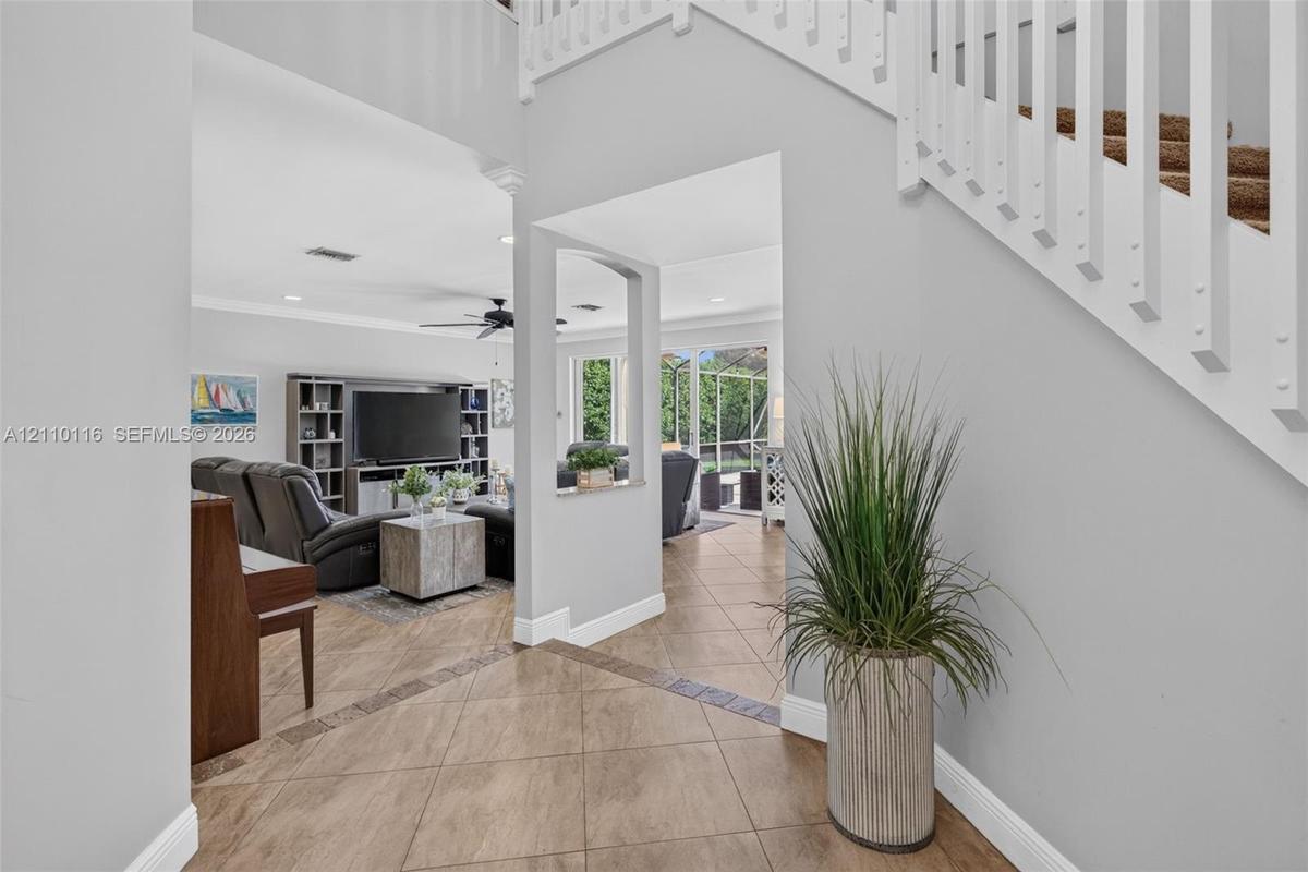 Two-story foyer featuring tile flooring with decorative inlay, a staircase with white balusters, and a pass-through window opening to the living area