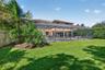 Rear exterior featuring a screened-in swimming pool enclosure, stucco siding, a tiled roof, and a manicured lawn