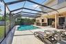 Screen-enclosed patio featuring a swimming pool, concrete pool deck, and a built-in outdoor bar with stone-finish siding