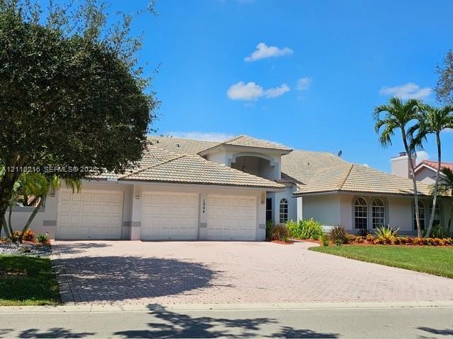 Single-story residence featuring a tile roof, three-car garage, arched window accents, and a paver driveway