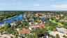 Aerial perspective of property featuring a multi-story residence with a tile roof, situated in a community with expansive water frontage and mature la