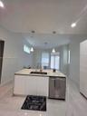 Kitchen island with a light-toned stone-patterned countertop, double-basin undermount sink, integrated stainless steel dishwasher, sleek white cabinet