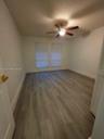 Room featuring wood-finish flooring, dual windows with blinds, a ceiling fan with integrated light fixture, and louvered closet doors