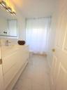 Bathroom featuring a modern white floating vanity with an integrated basin, polished metal faucet, multi-bulb vanity lighting, and light-toned tile fl