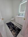 Bathroom featuring a white vanity cabinet with a integrated sink, LED-backlit mirror, and light-toned tile flooring