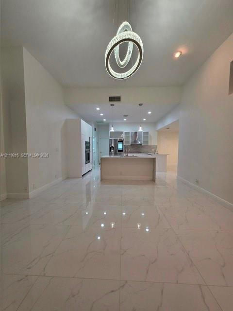 Large-format porcelain tile flooring with veining detail, central island with waterfall edge, recessed ceiling lighting, and sculptural multi-ring pen