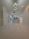 Large-format porcelain tile flooring with veining detail, central island with waterfall edge, recessed ceiling lighting, and sculptural multi-ring pen