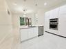 Modern kitchen featuring floor-to-ceiling white cabinetry, stone-finish countertops, stainless steel double wall ovens, a central island with an integ