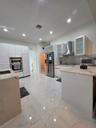 Kitchen featuring white cabinetry, stone-finish countertops, large-format tile flooring, a stainless steel range hood, and integrated wall ovens
