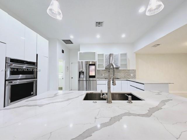 Kitchen featuring a large waterfall-edge island with stone-surface countertop, high-gloss flat-panel cabinetry, stainless steel double wall oven, stai