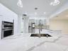 Kitchen featuring a large waterfall-edge island with stone-surface countertop, high-gloss flat-panel cabinetry, stainless steel double wall oven, stai