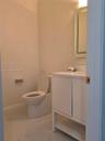 Bathroom featuring stone-finish floor tile, white vanity with integrated basin, back-lit wall mirror, and modern toilet