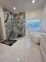 Walk-in shower with floor-to-ceiling patterned stone tile, glass enclosure, and rainfall showerhead, complemented by a freestanding soaking tub, glass