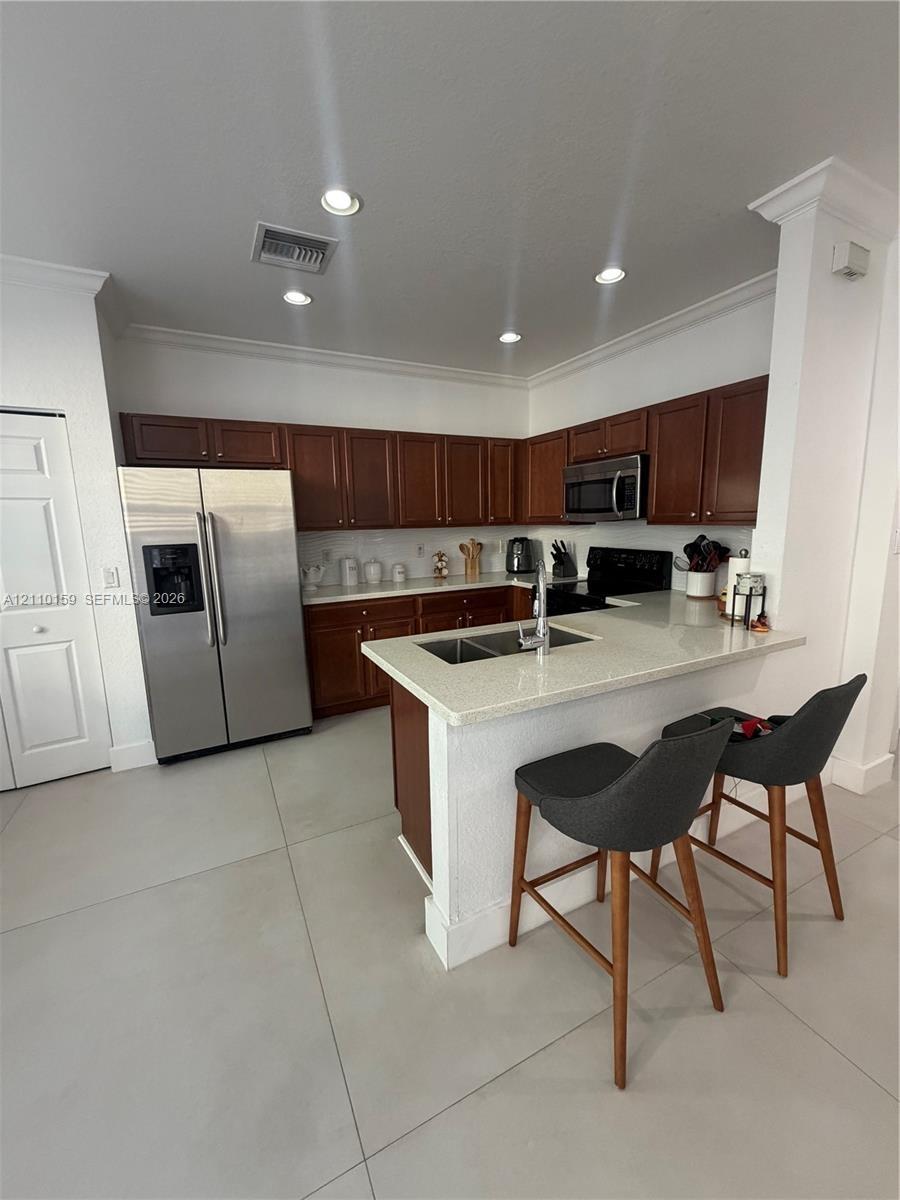 Kitchen featuring stained wood cabinetry, stone-finish countertops, stainless steel refrigerator, recessed lighting, and a breakfast bar