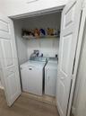 Laundry closet featuring white bi-fold doors, white top-load washer and dryer, and wire shelving