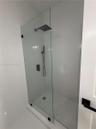 Walk-in shower featuring a frameless glass panel, matte black wall-mounted fixtures, a square rain-style showerhead, and a hand-held sprayer