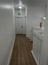 Hallway featuring wood-finish flooring, white six-panel interior doors, and a painted wooden railing