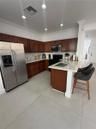 Kitchen featuring wood cabinetry, light-toned stone countertops, a center island with a dual-basin stainless steel sink, large-format tile flooring, a