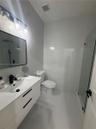 Bathroom featuring a white geometric-pattern vanity, rectangular vessel sink, matte black faucet, wall-mounted rectangular mirror, and glass-enclosed 
