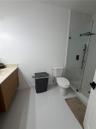 Bathroom featuring light-toned wood-finish vanity, solid surface countertop, walk-in shower with glass enclosure, and matte black shower fixtures