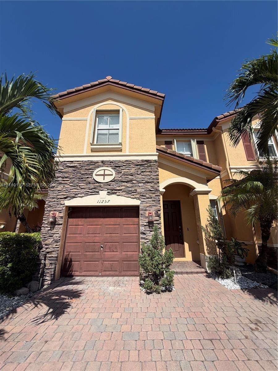 Two-story exterior featuring a stone veneer facade, a tiled roof, a brick-paver driveway, and an arched entryway