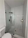 Walk-in shower featuring a frameless glass partition, matte black rainfall showerhead, handheld sprayer, and hexagon tile floor