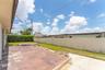 Rear exterior space featuring a paved patio, elevated platform area, lawn, and perimeter masonry wall with hedge landscaping