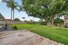 Spacious backyard featuring a wood deck, manicured lawn, perimeter wood fencing, and mature trees