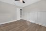 Room featuring white wainscoting, wood-finish flooring, a ceiling-mounted light fixture with a fan, and a closet with built-in shelving