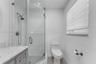Walk-in shower featuring white subway tile surround, glass enclosure, and hand-held shower fixture, paired with a stone-top vanity and one-piece toile
