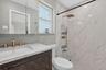 Bathroom featuring a vanity with wood-finish cabinetry, a light-toned stone countertop, brass-finish fixtures, a shower enclosure with large-format st